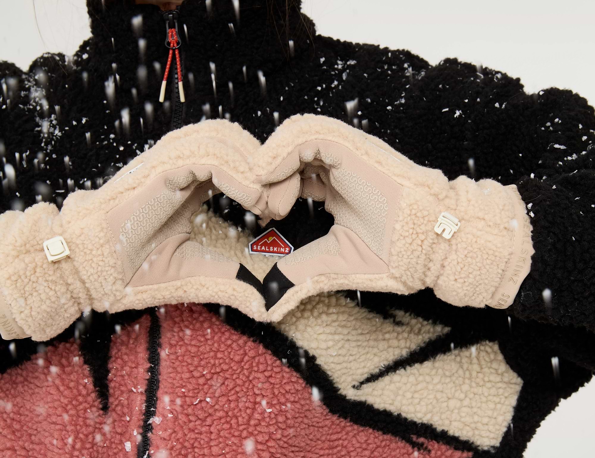 Women with fleece gloves and a pink mountain print jumper making a heart with her hands in the snow